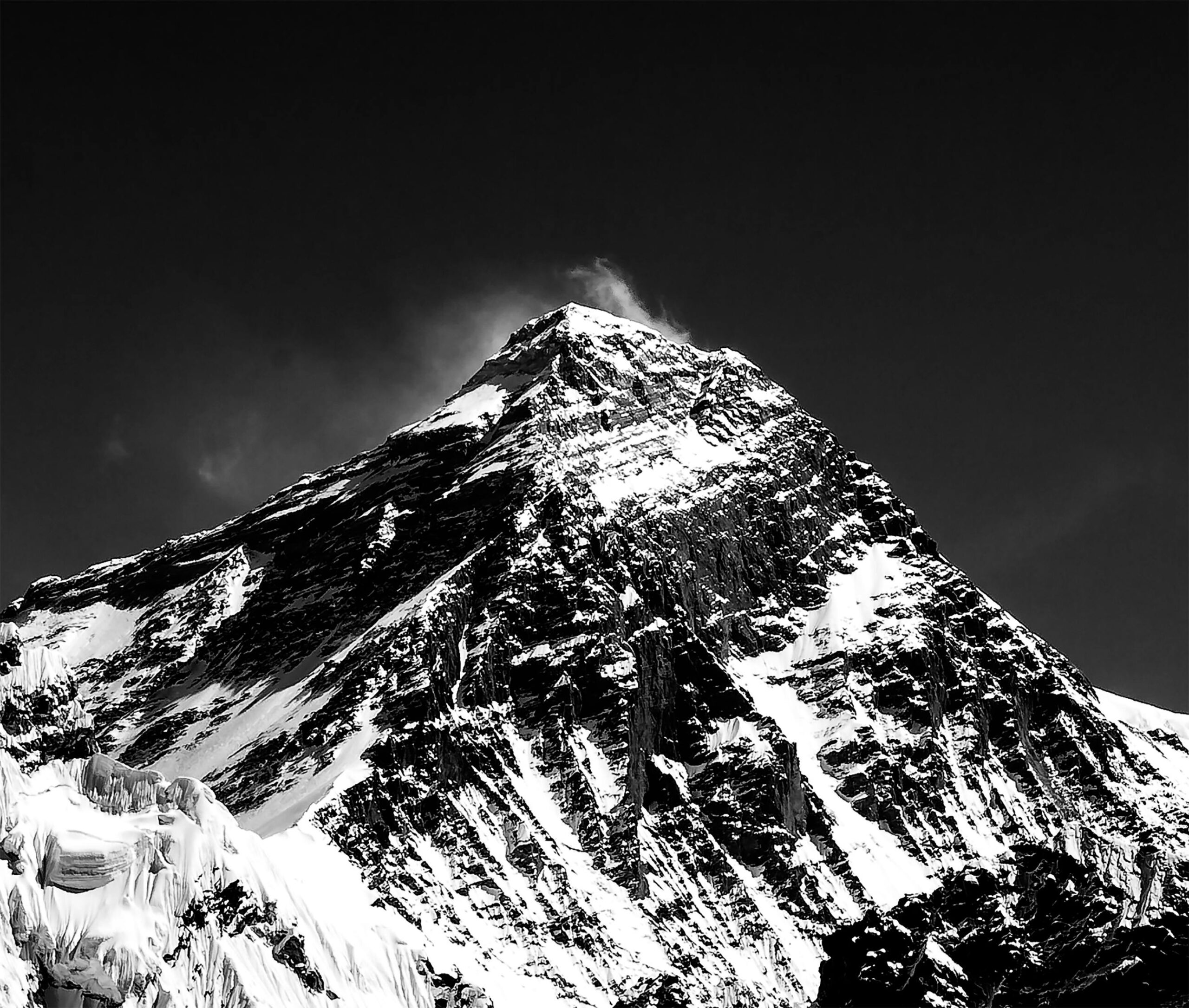 Dramatic black and white photograph of snow-capped Mount Everest under clear skies.